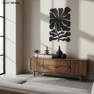 Peut inclure: Une d&eacute;coration murale florale en m&eacute;tal noir est suspendue au-dessus d'un meuble en bois. Le meuble a un design moderne du milieu du si&egrave;cle. Une petite plante en pot, des livres et des objets d&eacute;coratifs sont plac&eacute;s sur le dessus.