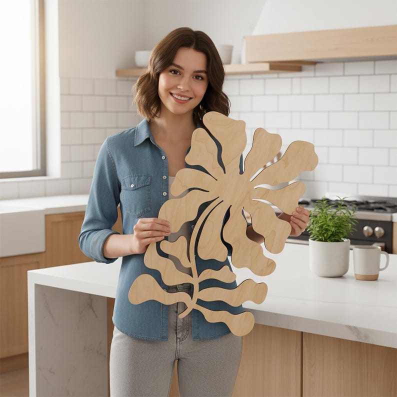 Peut inclure: Une grande &oelig;uvre d'art murale en bois clair en forme de fleur stylis&eacute;e. L'&oelig;uvre est tenue par une personne dans une cuisine. La pi&egrave;ce a une finition en grain de bois naturel et un design d&eacute;coup&eacute;, adapt&eacute; &agrave; la d&eacute;coration int&eacute;rieure.