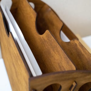 K&ouml;nnte beinhalten: Ein h&ouml;lzerner Schreibtisch-Organizer mit warmbraunem Finish. Der Organizer hat mehrere F&auml;cher mit geschwungenen Aussparungen und enth&auml;lt wei&szlig;es Papier. Das Design ist einfach und funktional, geeignet f&uuml;r B&uuml;ro oder Zuhause.