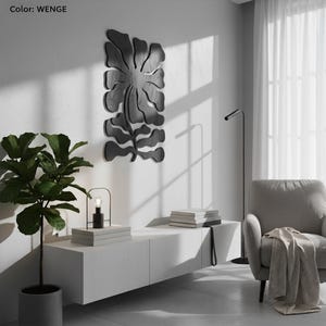 Peut inclure: Une &oelig;uvre d'art murale en bois noir en forme de fleur et de feuilles stylis&eacute;es. L'&oelig;uvre est fix&eacute;e sur un mur blanc. Le mot "WENGE" est dans le coin sup&eacute;rieur gauche. Un meuble blanc, une lampe et une plante en pot sont au premier plan.
