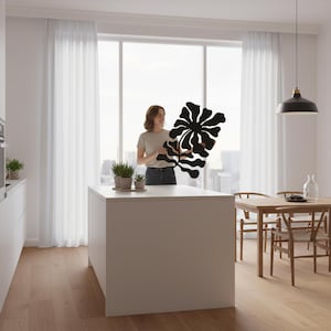 Peut inclure: Une &oelig;uvre d'art murale florale noire et abstraite est pr&eacute;sent&eacute;e dans une cuisine lumineuse et moderne. L'&oelig;uvre a une forme organique unique. La cuisine comprend un &icirc;lot blanc, des planchers en bois et un coin repas.