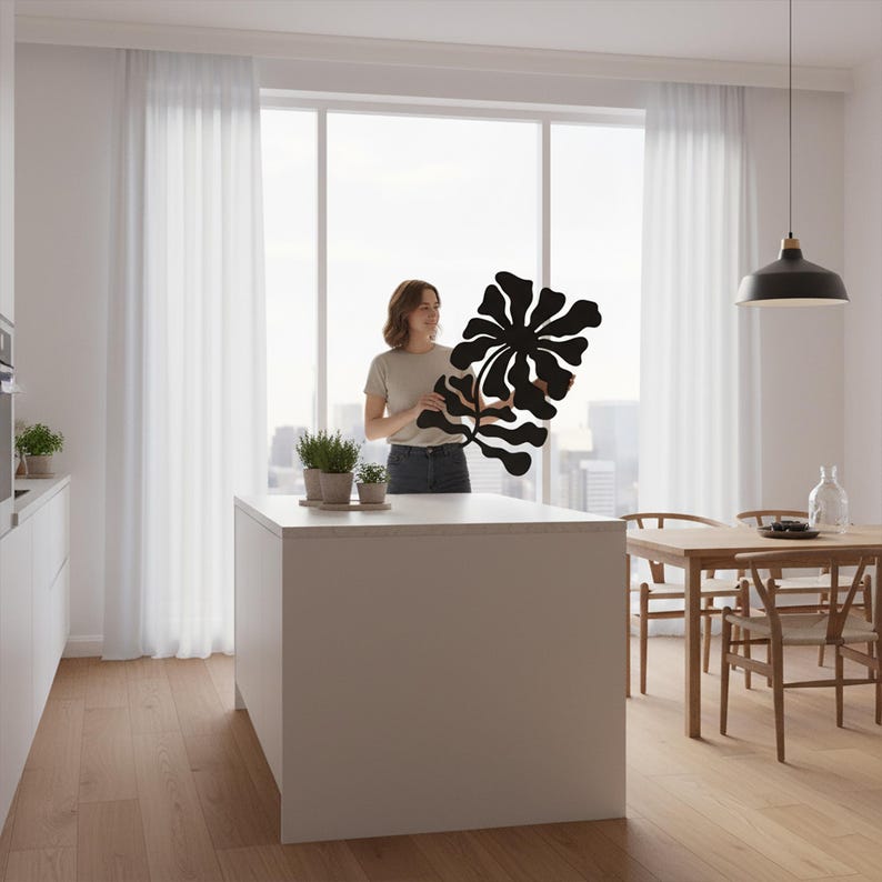 Peut inclure: Une &oelig;uvre d'art murale florale noire et abstraite est pr&eacute;sent&eacute;e dans une cuisine lumineuse et moderne. L'&oelig;uvre a une forme organique unique. La cuisine comprend un &icirc;lot blanc, des planchers en bois et un coin repas.
