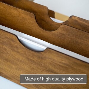K&ouml;nnte beinhalten: Nahaufnahme eines Weinregals aus Holz mit gebogenen Schlitzen. Das Regal besteht aus braunem Sperrholz und hat einen hellen Innenraum. Der Text "Made of high quality plywood" wird unten angezeigt.