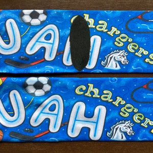 May include: A pair of blue socks with a white background. The socks feature a variety of colorful designs, including a basketball, a soccer ball, a rocket ship, a stethoscope, and a horse. The socks also have the name "UAH" written in large, white letters.