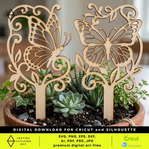 Op de afbeelding: Twee houten vlinder plantenprikkers. Elke prikker heeft een vlinderontwerp met ingewikkelde uitgesneden details, tegen een achtergrond van groen in een terracotta pot. De prikkers zijn gemaakt van lichtgekleurd hout. De afbeelding bevat ook tekst met de tekst "DIGITALE DOWNLOAD VOOR CRICUT en SILHOUETTE".