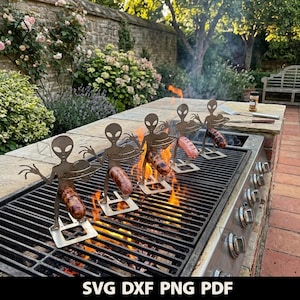 Può includere: Quattro spiedini in metallo a forma di alieno su una griglia nera sopra fiamme arancioni. Ogni figura tiene un piattino e ha una salsiccia marrone infilzata al centro. Il testo SVG DXF PNG PDF è visibile.
