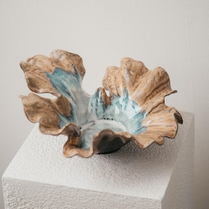 May include: A ceramic bowl with a ruffled, organic edge. The exterior and rim feature a tan, earthy brown glaze, while the interior is finished with a glossy, vibrant turquoise and white drip glaze that pools at the centre of the vessel.