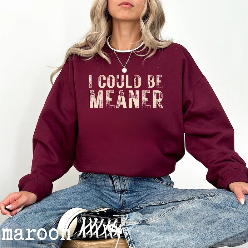 May include: Maroon sweatshirt with the text "I COULD BE MEANER" in a distressed, off-white font. The sweatshirt has a crew neck and long sleeves. The word "maroon" is printed at the bottom left corner of the image.