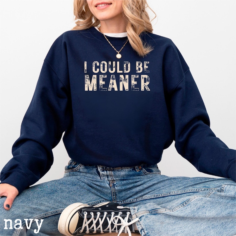 May include: Navy blue sweatshirt with the text "I COULD BE MEANER" in a distressed, off-white font. The sweatshirt is a long-sleeved crew neck. The word "navy" is printed at the bottom left of the image.