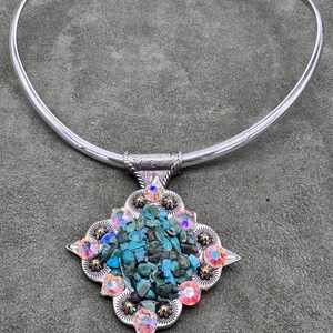 May include: A silver choker necklace with a square pendant featuring turquoise stones and iridescent rhinestones.