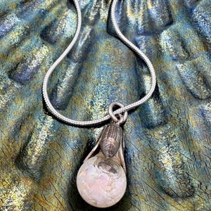 May include: A silver chain necklace with a pendant featuring a clear glass orb filled with iridescent glitter and a silver cap.