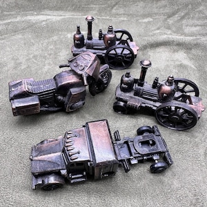 May include: Four vintage metal pencil sharpeners in the shape of a motorcycle, a truck, and two steam engines. The sharpeners are all in a bronze color and have a worn look.