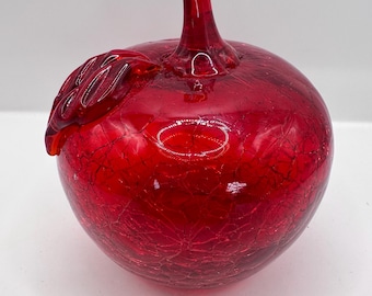 May include: A red glass apple with a textured surface and a small leaf detail. The apple is a decorative object.