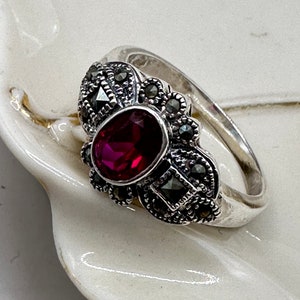 May include: A silver ring with a large oval-shaped red gemstone surrounded by smaller black gemstones.