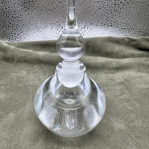 May include: A clear glass bottle with a textured surface and a tall, pointed stopper. The bottle has a unique, layered design.