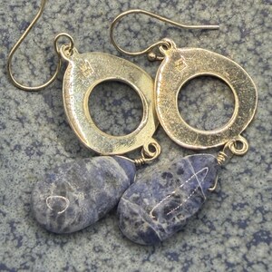 May include: Silver drop earrings with teardrop-shaped blue sodalite stones. The earrings have a circular design with a small loop at the top for the ear wire. The sodalite stones are a deep blue with white marbling.