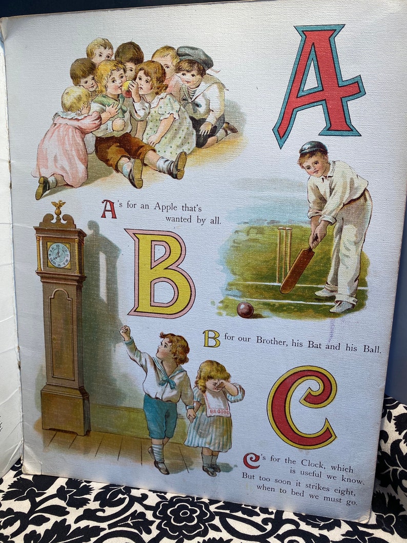 May include: An illustrated alphabet book with colorful letters and images. The letter A is red with a blue outline and shows a boy playing cricket. The letter B is yellow with a red outline and shows a boy and girl standing next to a clock. The letter C is red with a yellow outline and shows a clock.