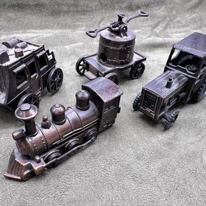 May include: Four vintage metal toy vehicles: a stagecoach, a train engine, a small crane, and a tractor. All are painted in a dark brown color.