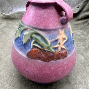 May include: A pink and blue ceramic vase with a floral design. The vase has two handles and a rounded body.
