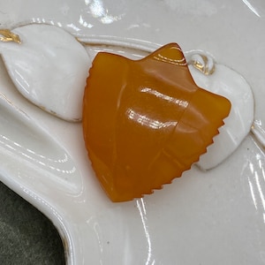 May include: A close-up of a decorative amber-colored object with a jagged edge, resting on a white ceramic surface with gold accents. The object has a unique, abstract shape, possibly a leaf or petal.