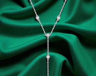 May include: A silver-toned Y-shaped necklace with multiple clear, round gemstones. The necklace is displayed against a backdrop of deep green fabric, creating a contrast that highlights the jewelry's sparkle. The gemstones are evenly spaced along the chain.