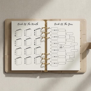 May include: Open planner with pages labelled "Book Of The Month" and "Book Of The Year." The left page has book icons for each month. The right page features a bracket for "Book Of The Year." The planner is beige with gold-coloured rings.