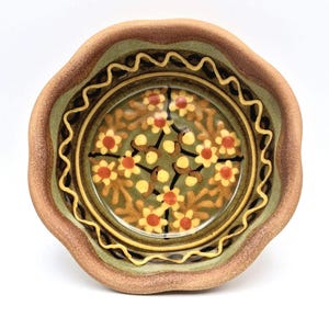 May include: A ceramic bowl with a wavy edge. The bowl has a floral pattern in the centre, with yellow and orange flowers on a green base. The rim has a brown and green colour scheme.