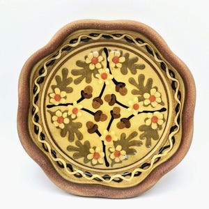 May include: A ceramic plate with a scalloped edge. The plate has a central floral design in yellow, brown, and orange, with a dark brown border and rim. The plate is likely 20 cm in diameter.