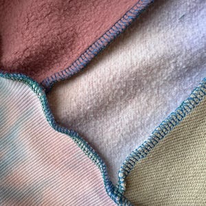 Puede incluir: Primer plano de una tela de patchwork con varias texturas y colores. La imagen muestra secciones de telas rosas, te&ntilde;idas con tinte y gris claro, cosidas con hilo azul. Las texturas var&iacute;an de lisas a afelpadas.