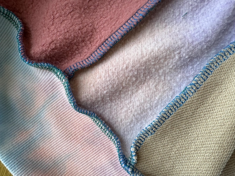 Puede incluir: Primer plano de una tela de patchwork con varias texturas y colores. La imagen muestra secciones de telas rosas, te&ntilde;idas con tinte y gris claro, cosidas con hilo azul. Las texturas var&iacute;an de lisas a afelpadas.