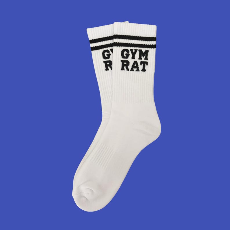 K&ouml;nnte beinhalten: Ein Paar wei&szlig;e Sportsocken mit schwarzen Streifen am oberen Rand und dem schwarzen Aufdruck "GYM RAT". Die Socken bestehen aus einem weichen, gerippten Material und sind auf Komfort und Leistung ausgelegt.