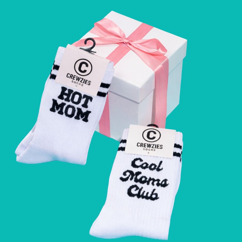 May include: White socks with black stripes and the text "HOT MOM" and "Cool Moms Club". The socks are displayed with a white gift box tied with a pink ribbon. The socks are from Crewzies Socks.