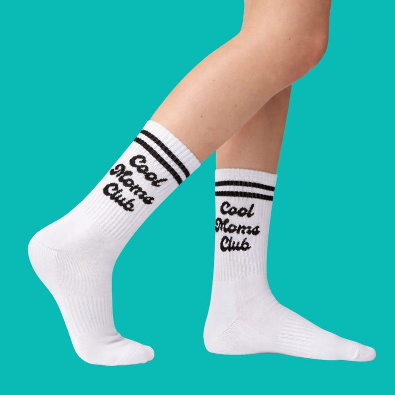 May include: White athletic socks with black stripes and the text "Cool Moms Club" in black. The socks are ribbed and reach mid-calf. The background is a solid teal color.
