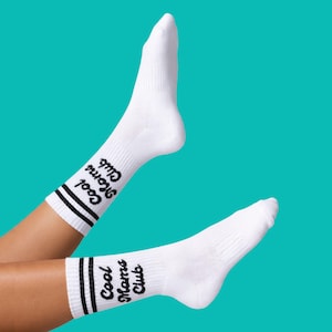 May include: White athletic socks with black stripes and the text "Cool Moms Club" in a script font. The socks are against a teal background.
