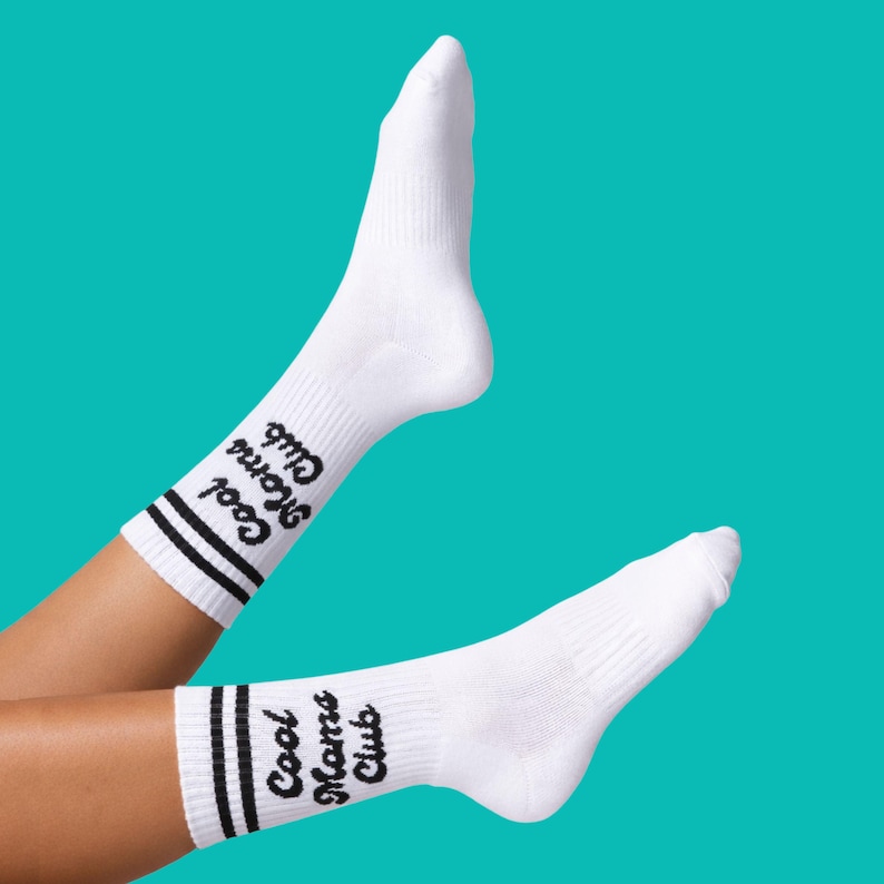 May include: White athletic socks with black stripes and the text "Cool Moms Club" in a script font. The socks are against a teal background.