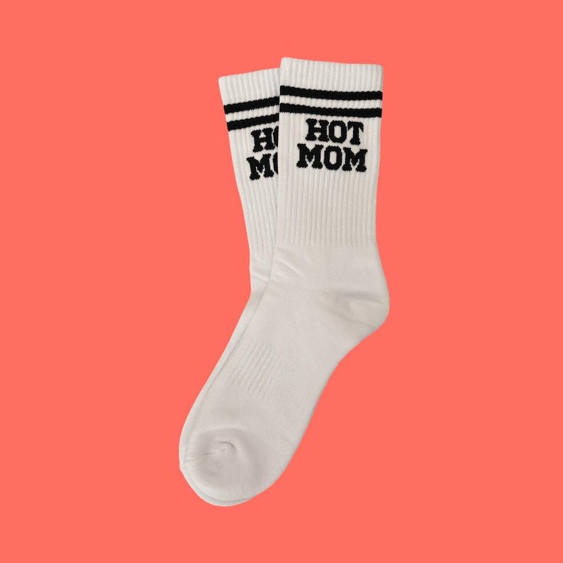 May include: A pair of white socks with black text that reads "HOT MOM" on one sock and "HOT MOM" on the other. Each sock has two black stripes at the top.