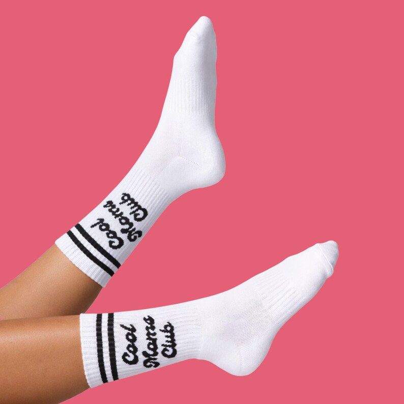 May include: White athletic socks with black stripes and the text "Cool Moms Club" in a script font. The socks are displayed against a pink background.