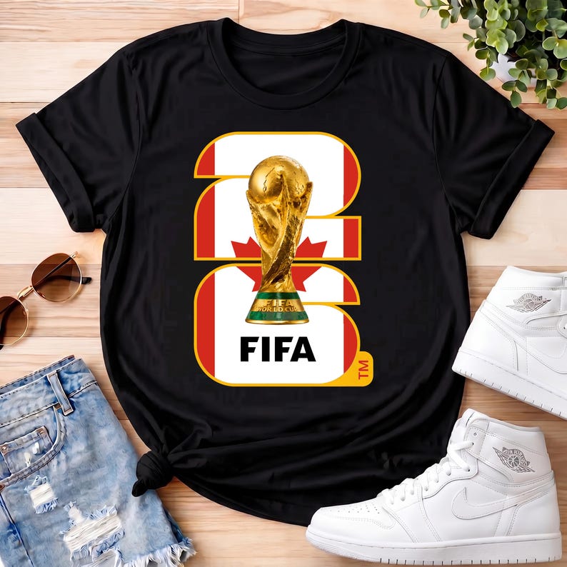 Może przedstawiać: Czarna koszulka z złotą grafiką trofeum FIFA World Cup. Projekt zawiera kanadyjską flagę i słowo "FIFA". Koszulka jest prezentowana z okularami przeciwsłonecznymi, dżinsowymi szortami i białymi trampkami.