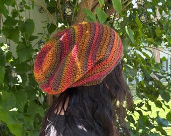 May include: A colorful, crocheted beret in shades of orange, red, brown, and green. The beret is made with a striped pattern and is worn on the head. The beret is a stylish accessory for any outfit.