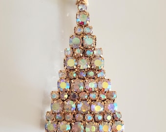 May include: A Christmas tree brooch with a gold-tone metal frame and iridescent, square-cut rhinestones. The tree is topped with a gold star and has a rectangular base. A festive holiday accessory.