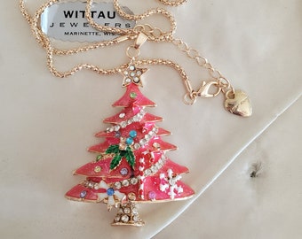 May include: A gold chain necklace with a pink, sparkly Christmas tree pendant. The pendant features a green bow, white snowflakes, and red and white candy canes. The necklace is in a white box with a pink lining. The box has a label that reads "Wittau Jewelers Marinette, Wis."