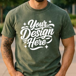 May include: Olive green t-shirt with the text "Your Design Here" in white script. The shirt has a crew neck and short sleeves. The model is wearing blue jeans.