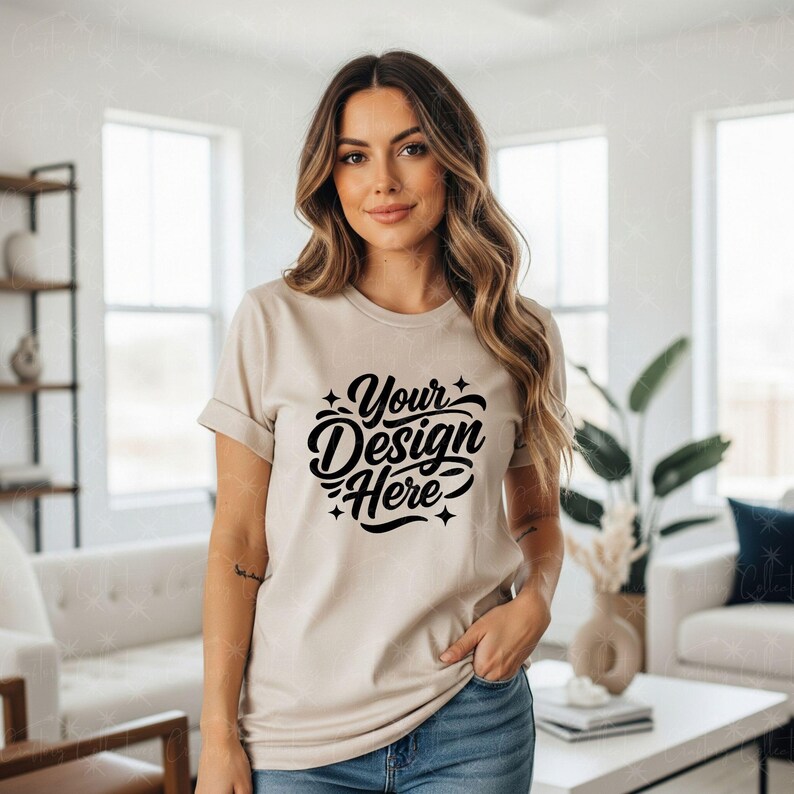 May include: A beige t-shirt with rolled-up sleeves featuring the text "Your Design Here" in a black, stylized script. The model is wearing blue jeans. The shirt is a mockup for custom designs.