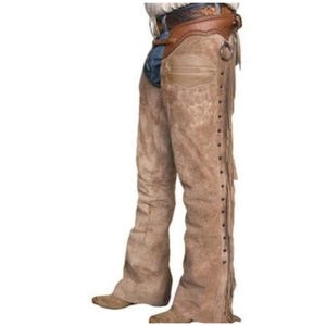 May include: Tan suede leather chaps featuring a dark brown leather waistband with a buckle closure, a smooth leather pocket detail on the upper thigh, and long fringe trim running down the outer side of each leg over blue denim jeans.