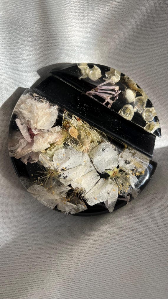 A phone stand cast with real pressed cherry blossoms and lily of the valley — the kind of botanical desk piece that looks like spring frozen in time.