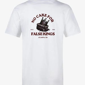 May include: White t-shirt with a graphic on the back. The graphic features a slice of cake with a crown, and the text "NO CAKE FOR FALSE KINGS ATLANTA, GA ESTD 2025" in maroon.