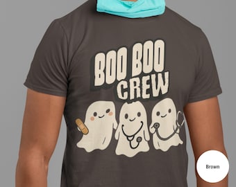 Pode incluir: Camiseta cinza escuro com o texto "BOO BOO CREW" acima de três fantasmas de desenho animado. Um fantasma tem um curativo, outro um estetoscópio e o terceiro um estetoscópio. A camiseta é de gola redonda.