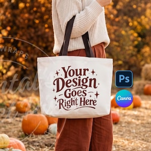 May include: A white canvas tote bag with dark brown handles featuring the maroon text Your Design Goes Right Here surrounded by small star icons. The bag is held in front of a field filled with orange pumpkins and autumn foliage.
