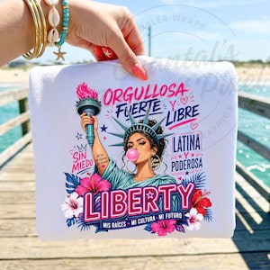 May include: White sweatshirt with a graphic of the Statue of Liberty blowing a bubble. The design includes the words "ORGULLOSA FUERTE Y LIBRE LATINA PODEROSA LIBERTY" and floral accents. The text "MIS RAÍCES MI CULTURA MI FUTURO" is also included.