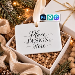 May include: A white rectangular ceramic ornament with rounded corners and a cream-colored ribbon loop. The ornament features black cursive text that reads Place DESIGN Here, accented by two small heart icons on either side of the word DESIGN.